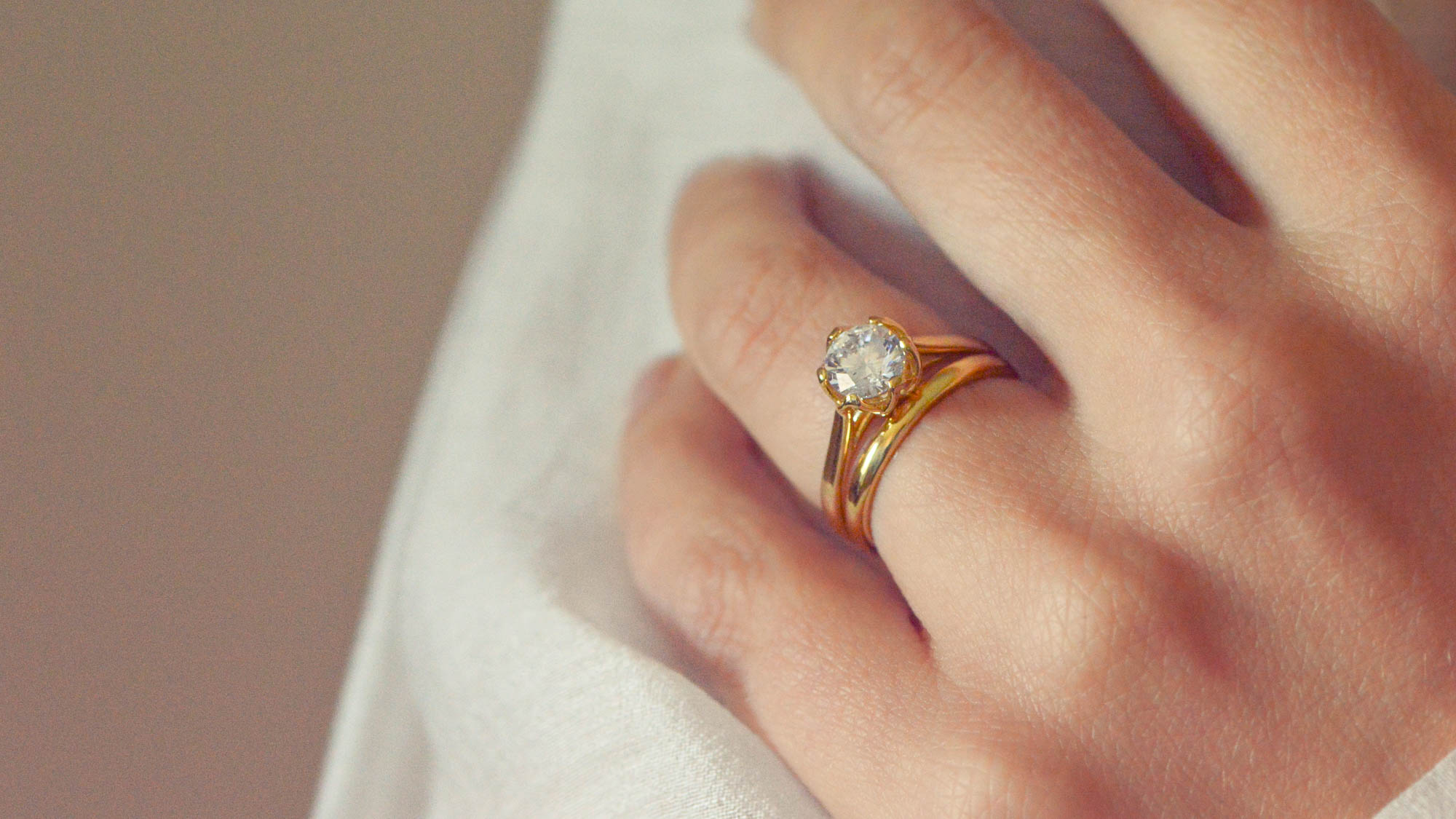 Close up of a round brilliant cut solitaire worn on the hand with a gold wedding band