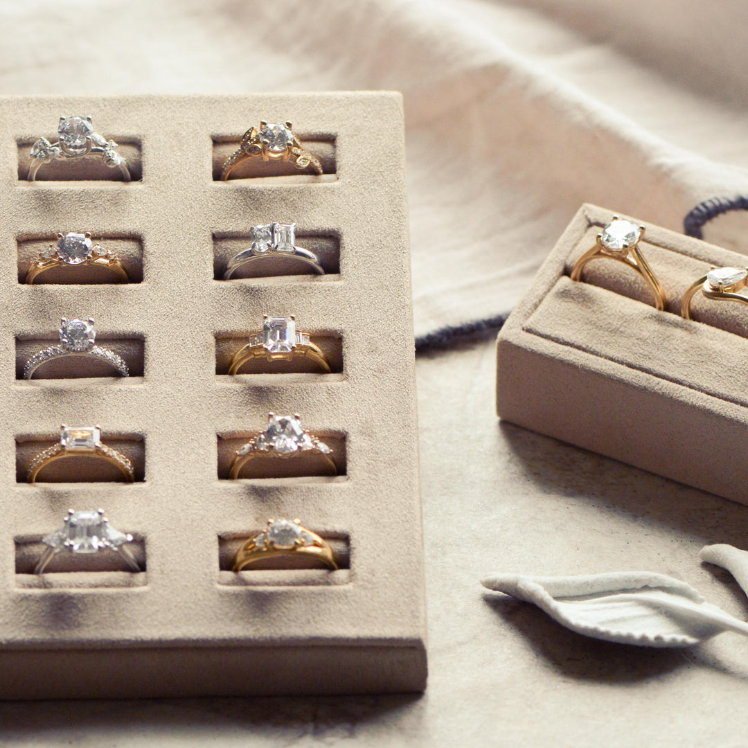 Display of gold and diamond rings in a beige jewelry box on a neutral background.