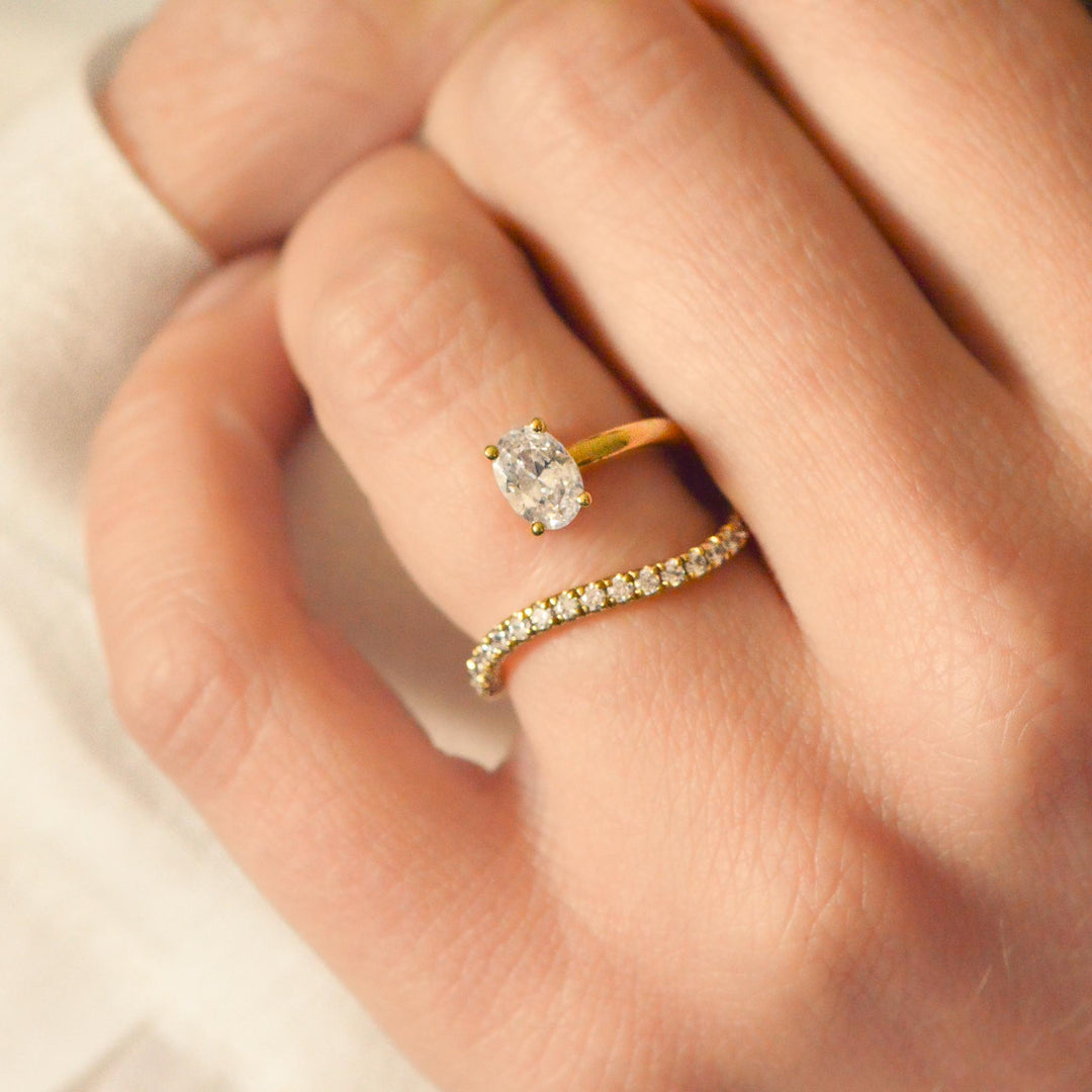 Gold ring with an oval cut diamond on a person's finger against a neutral background