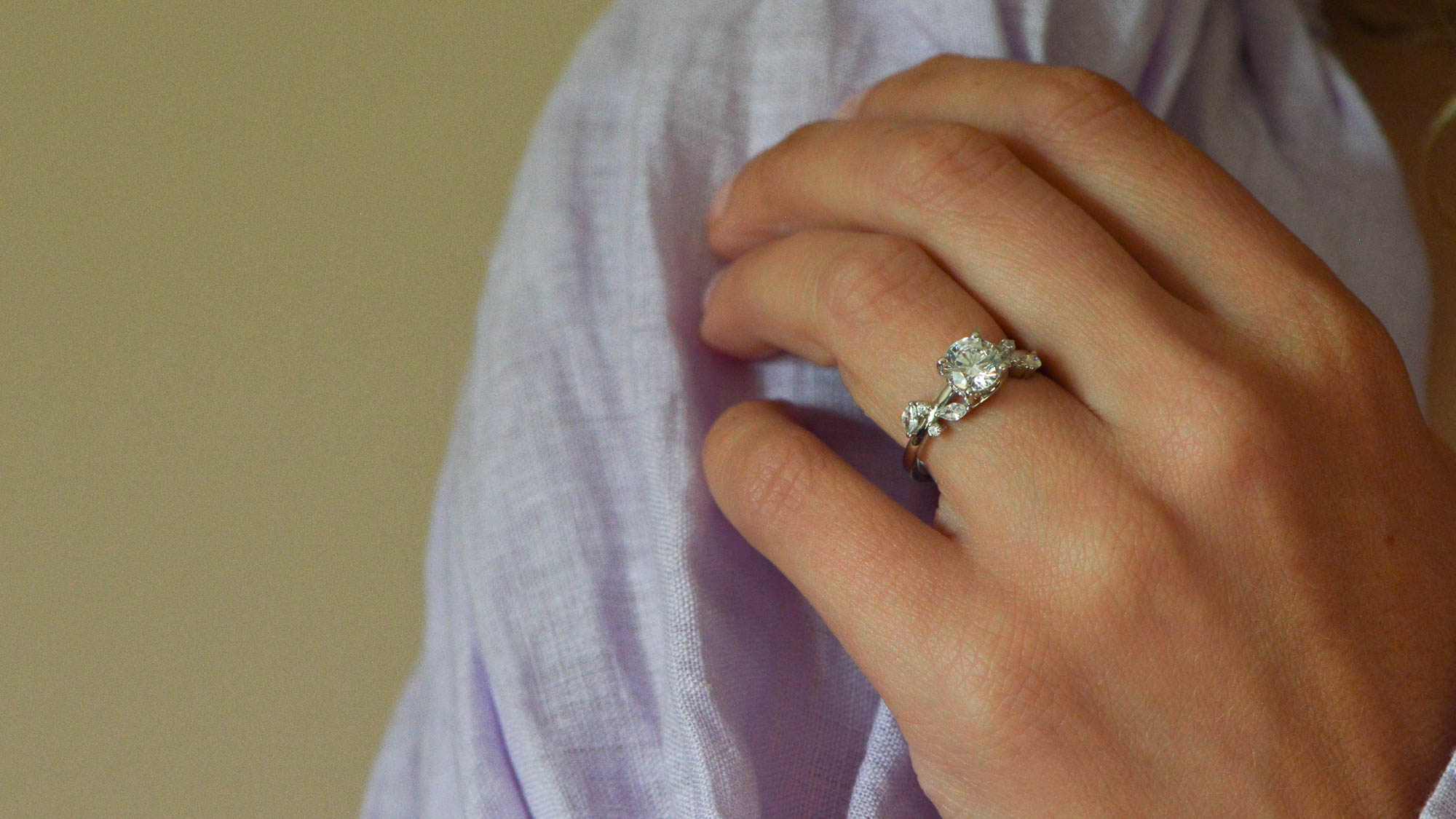 Hand wearing a platinum engagement ring with a round brilliant cut diamond on a blurred background
