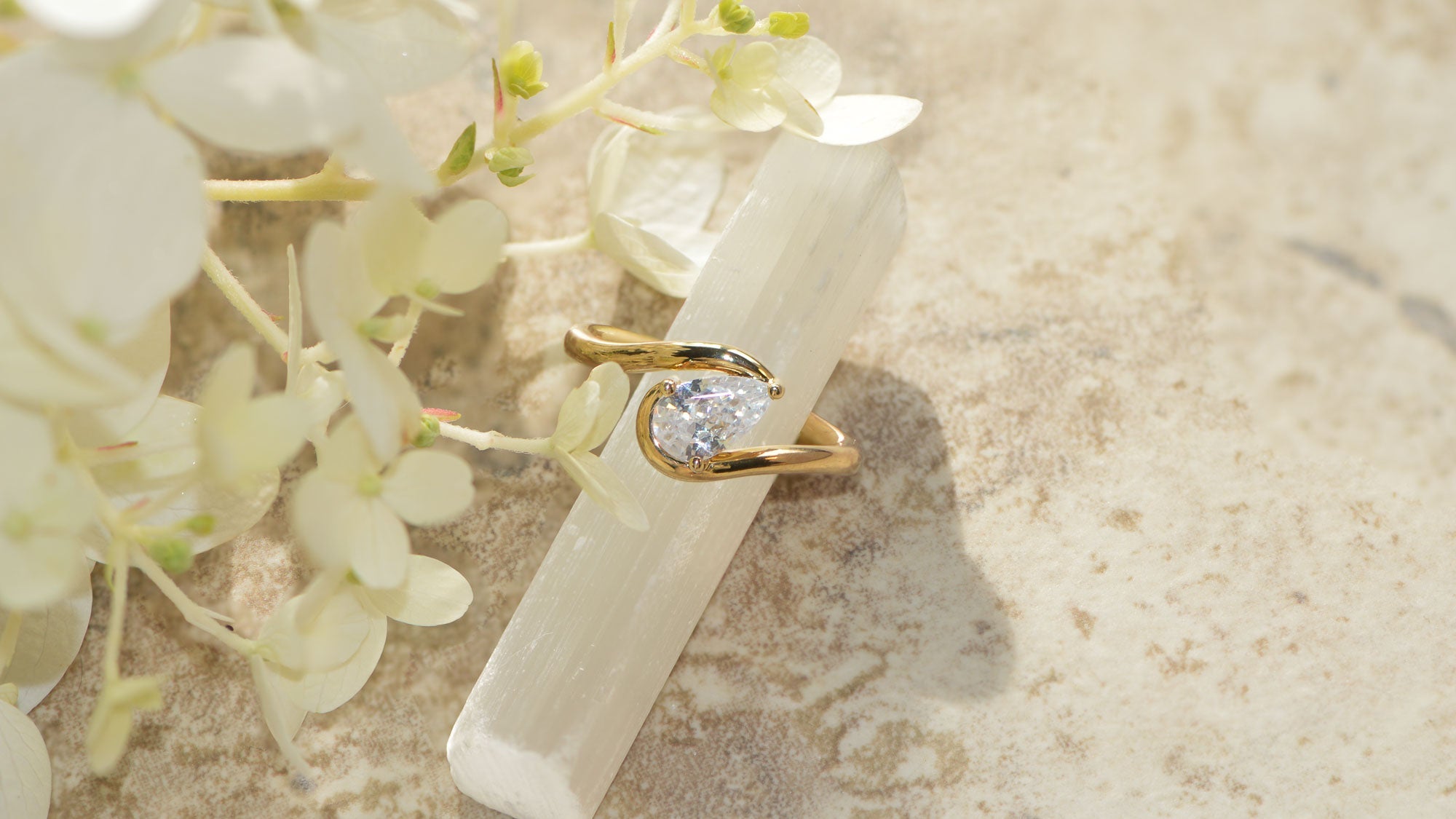 A modern solitaire engagement ring in yellow gold set with a pear cut diamond pictured on a marble background. 