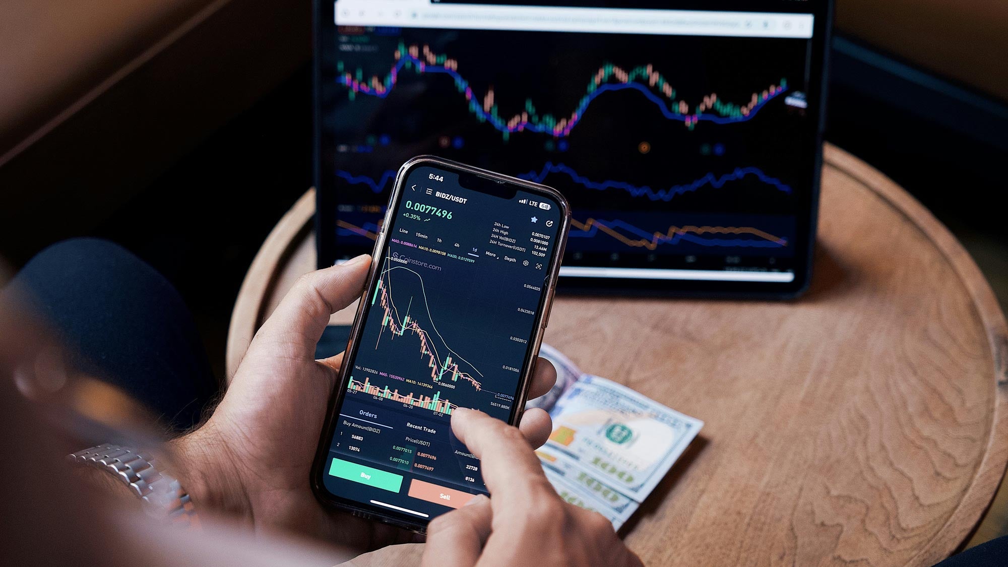 Person sat with a tablet on a coffee table and mobile phone in their hand with stocks and shares on both screens