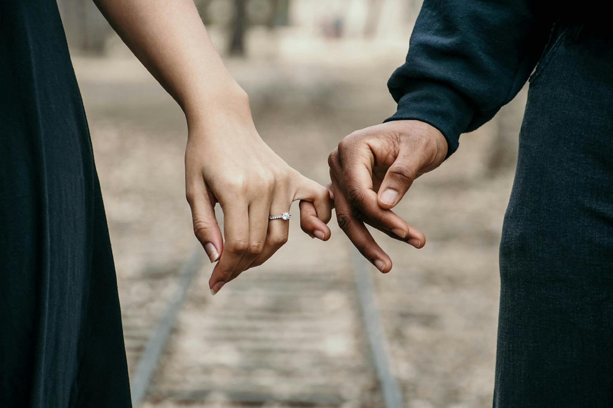 Two people walking side by side, one wears an engagement ring, with their fingers interlinked