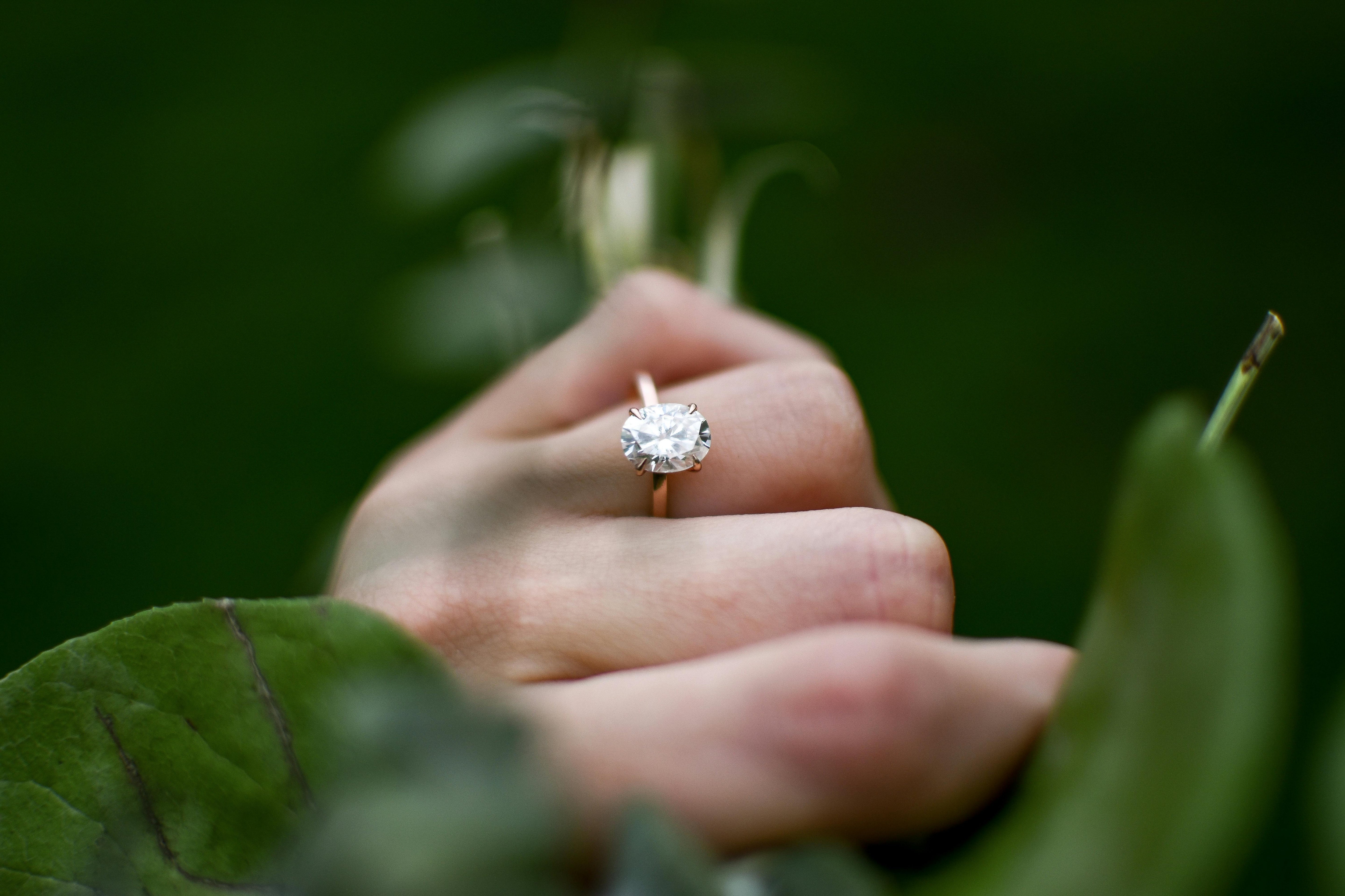 Large carat oval cut diamond ring on a woman's hand. Surrounded by soft focus, dark green leaves