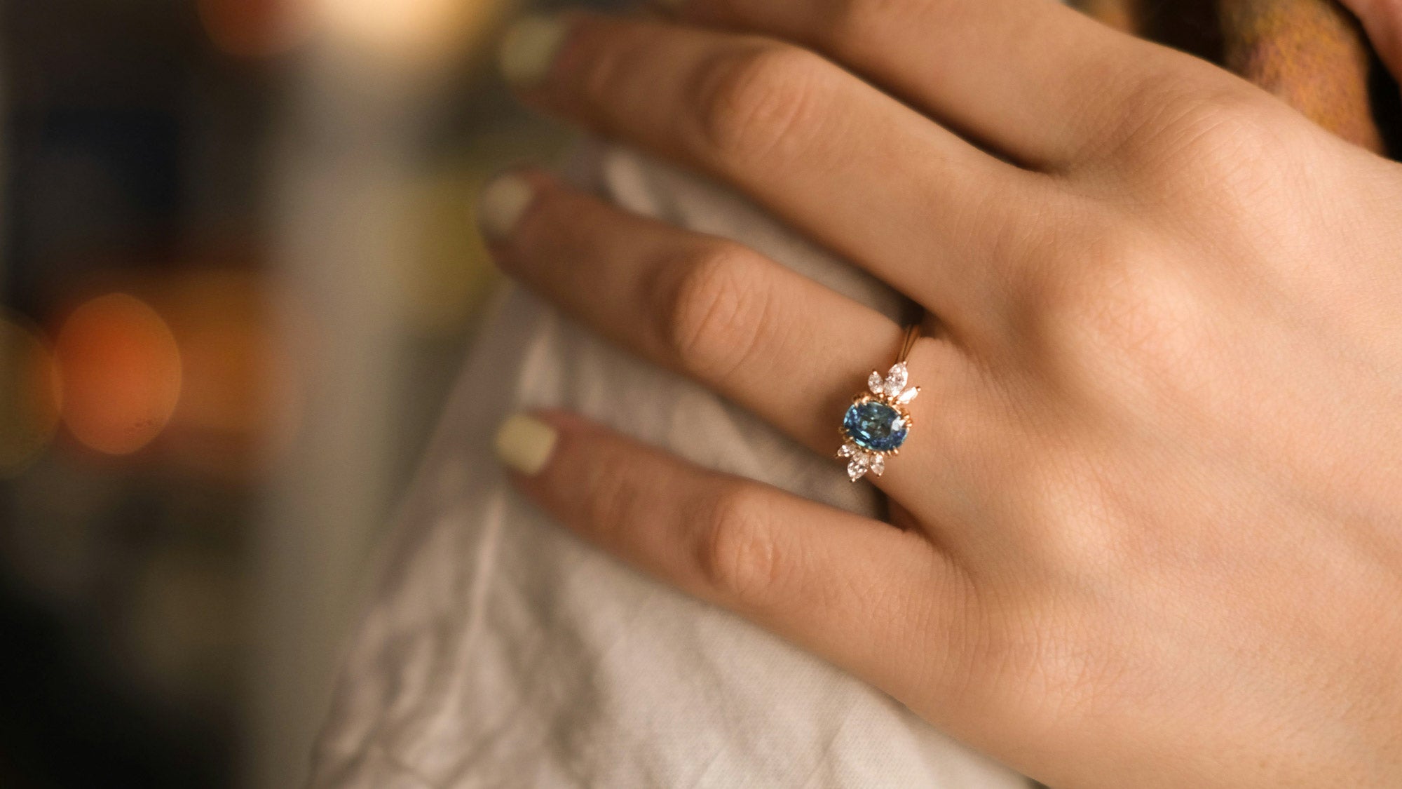 A blue stone engagement ring worn on the hand with a blurred background