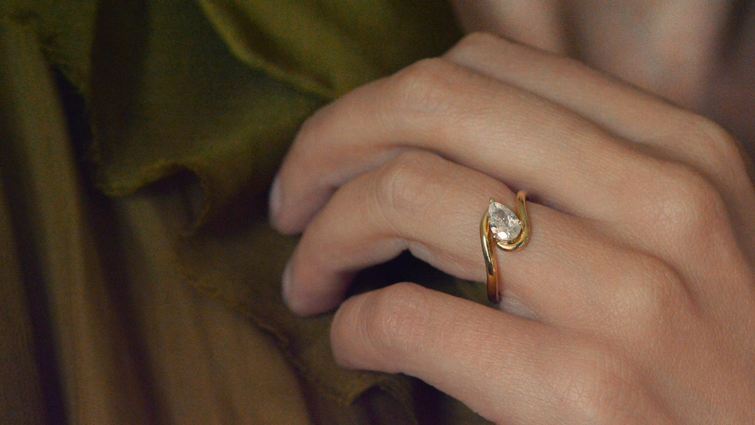 Pear cut diamond solitaire engagement ring with a pavé set chevron wedding band on a marble surface