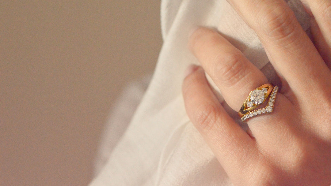 Close up of a gold trilogy engagement ring set with three diamonds. Worn on the hand with a soft focus purple background