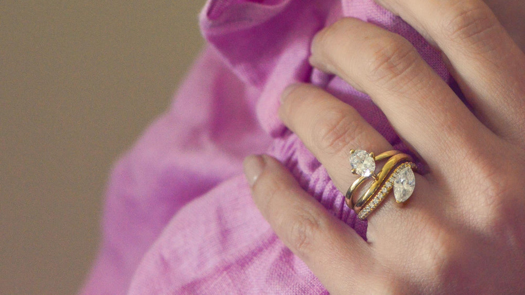 Close up of a hand wearing an oval cut solitaire engagement ring with a marquise cut diamond wedding band 