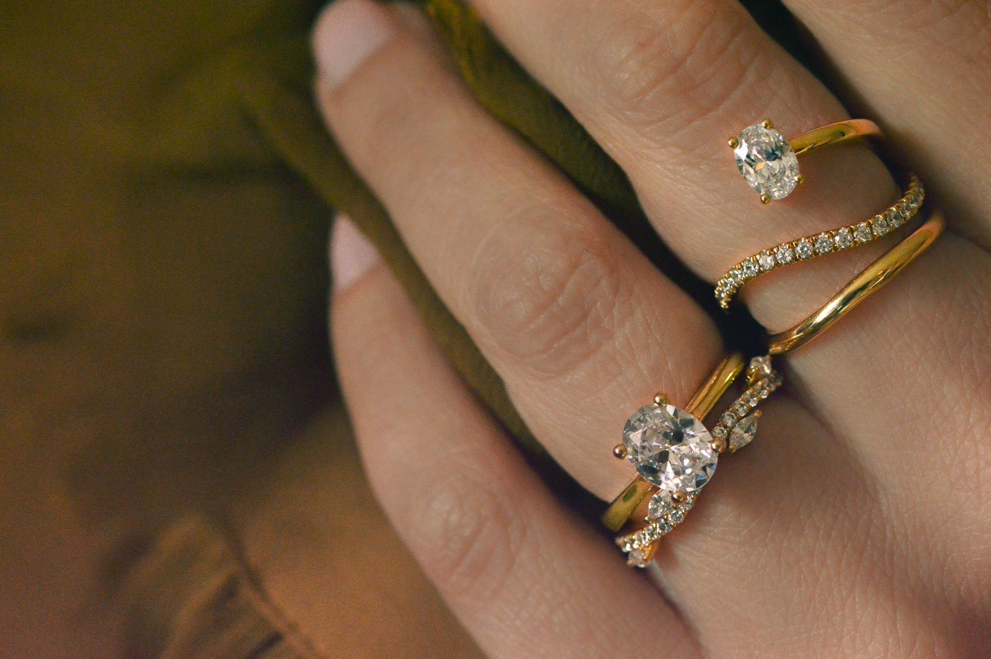 Collection of gold rings set with diamonds, worn on a hand with a dark background