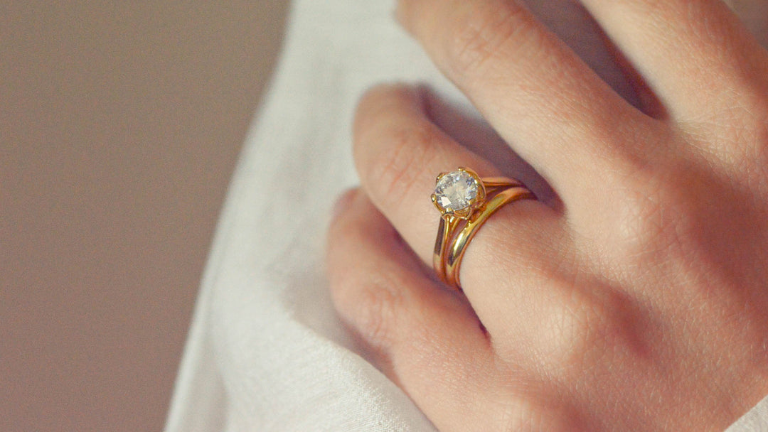 Close up of a round brilliant cut solitaire worn on the hand with a gold wedding band