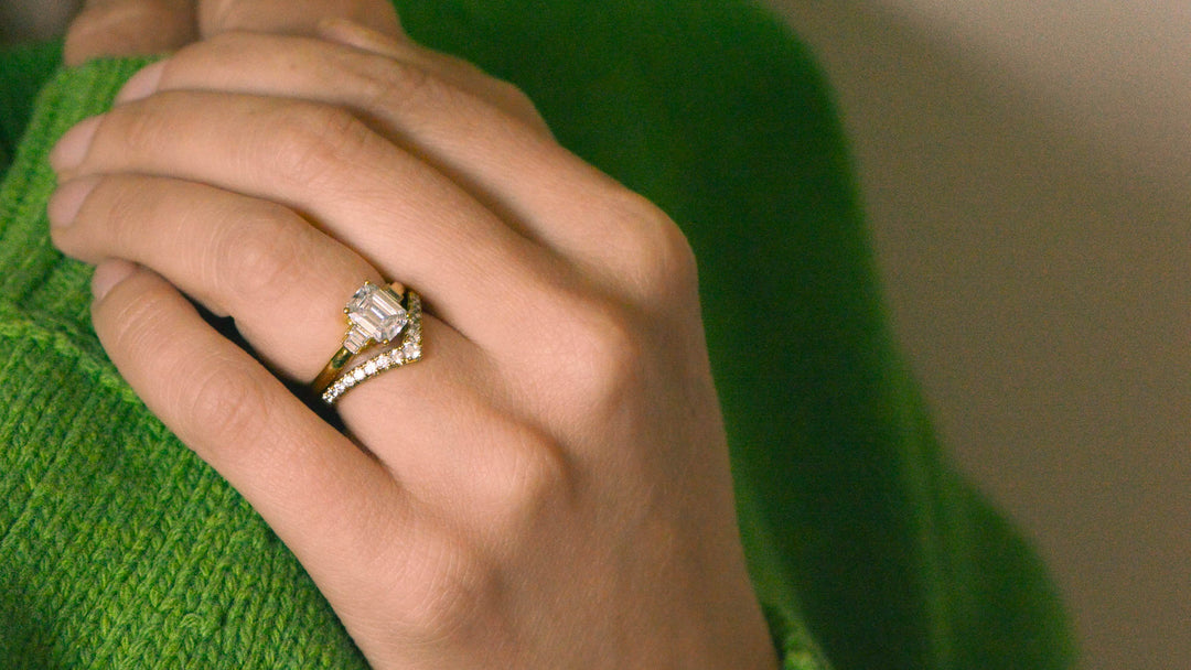 Emerald cut diamond Art Deco ring worn on the hand with a gold, pavé set chevron wedding band
