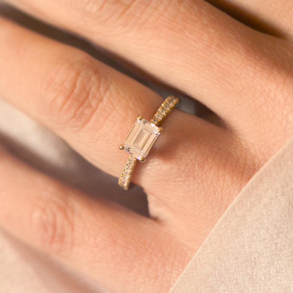 Gold east-west set ring with an emerald cut diamond on a finger