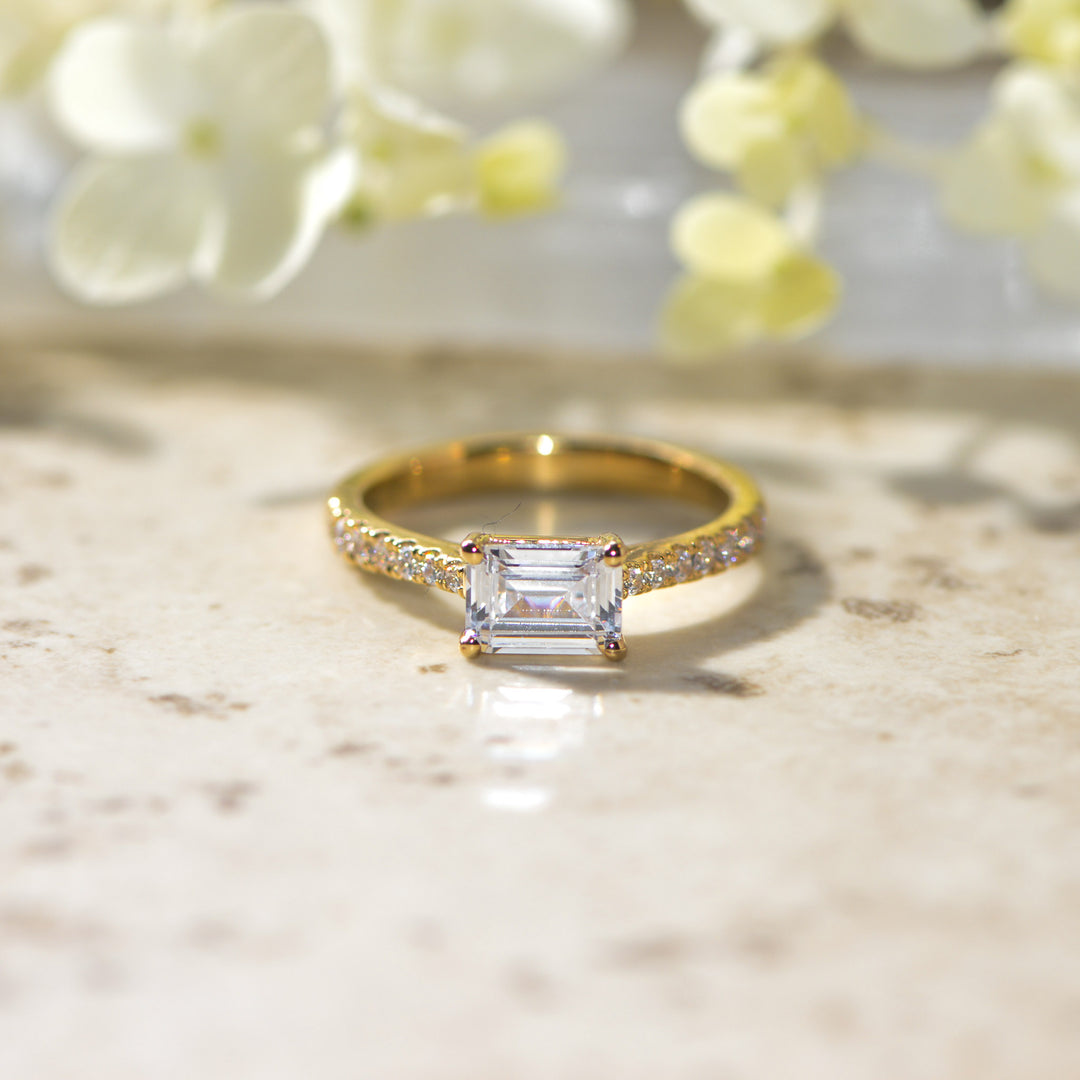 Gold ring with a diamond on a marble surface with flowers in the background