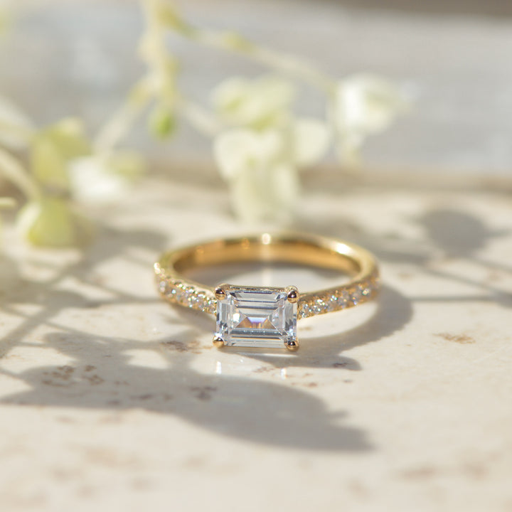 Gold ring with an east west set emerald cut diamond on a light background