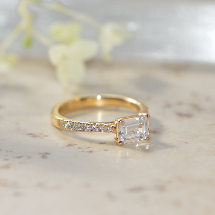 Gold shoulder set pavé ring with a diamond on a marble surface