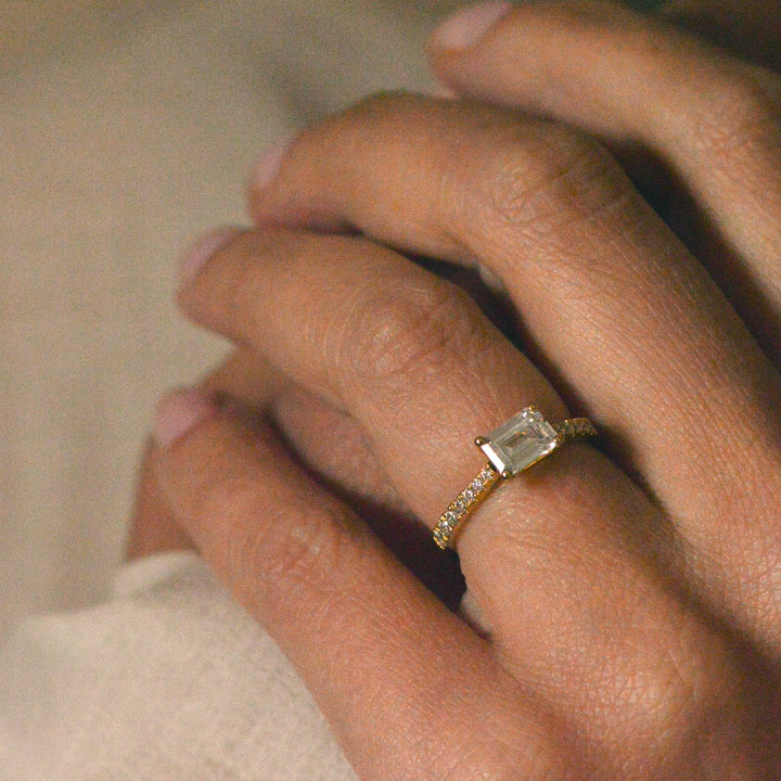 Close up of an emerald cut engagement ring with pavé shank worn on the hand 