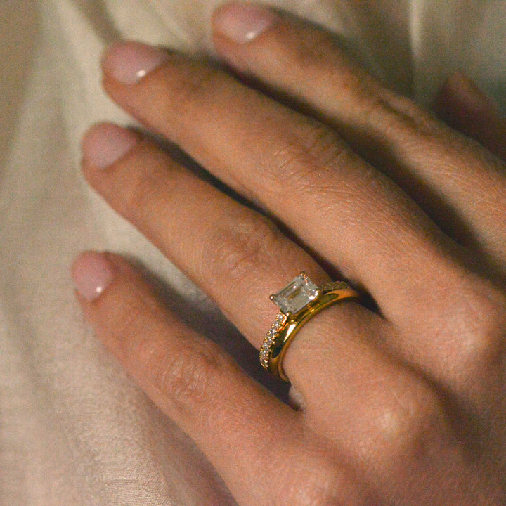 Emerald cut ring with a gold wedding band worn on the hand