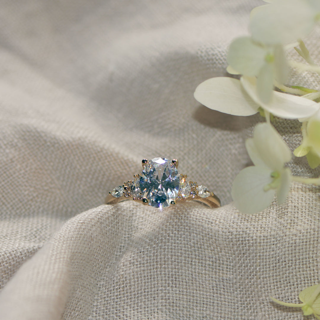 Oval cut gold ring with diamonds on a linen background with flowers