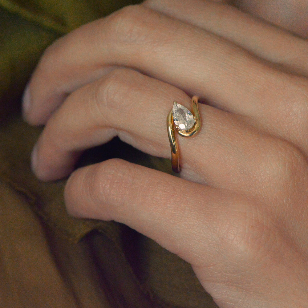 Gold pear cut diamond solitaire ring on a person's finger against a blurred background