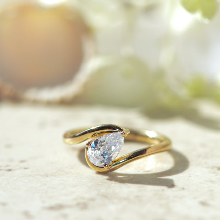 Gold ring with a pear cut diamond on a light background
