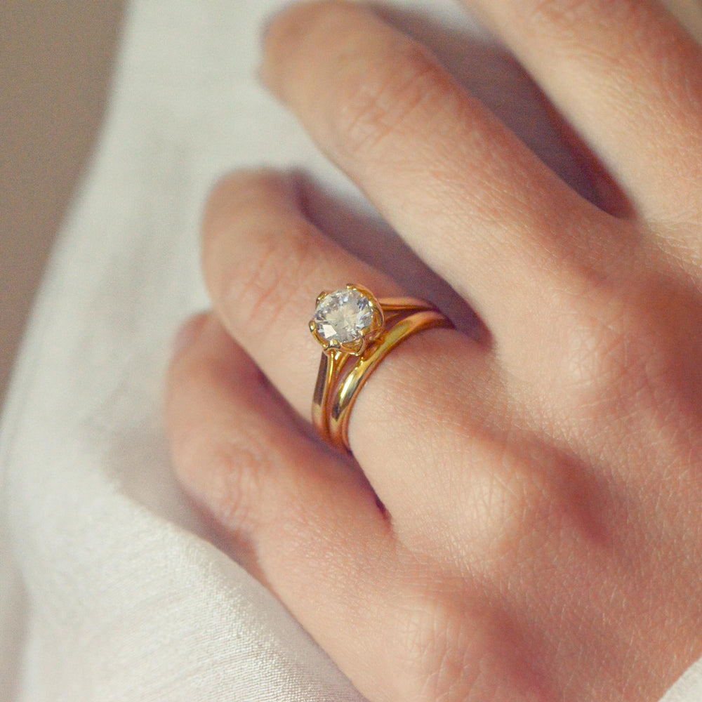 Gold ring with a diamond on a person's finger against a neutral background