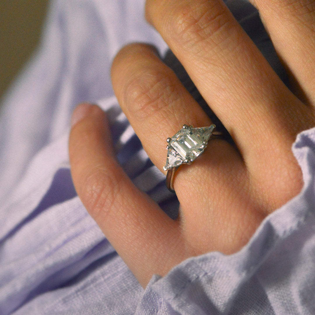 Close-up of a hand wearing a diamond trilogy ring with a soft focus background