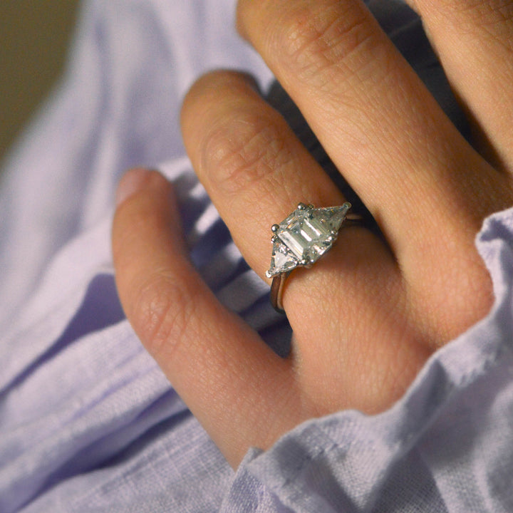 Close-up of a hand wearing a diamond trilogy ring with a soft focus background