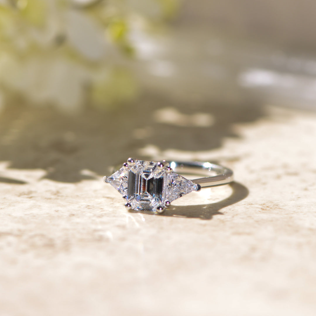 Three stone diamond platinum ring on a textured surface with a blurred natural background