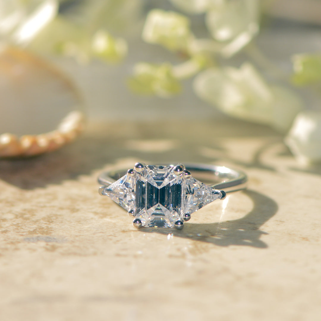 Diamond three stone ring on a textured surface with blurred greenery in the background