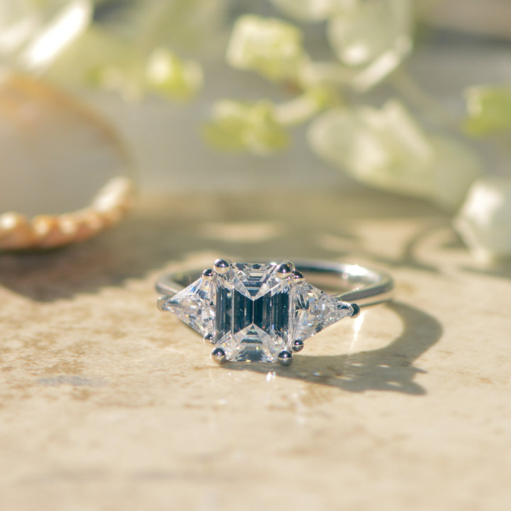 Diamond three stone ring on a textured surface with blurred greenery in the background