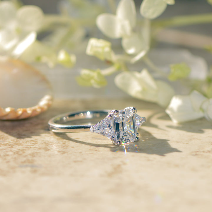 Diamond engagement ring with an emerald cut centre on a textured surface with floral background