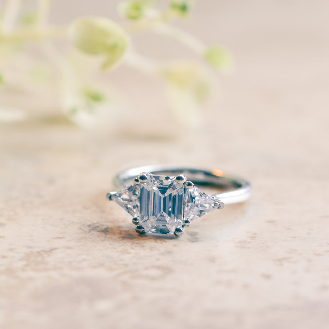 Emerald cut three stone engagement ring on a marble surface
