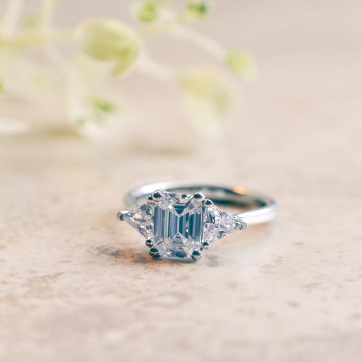 Emerald cut three stone engagement ring on a marble surface