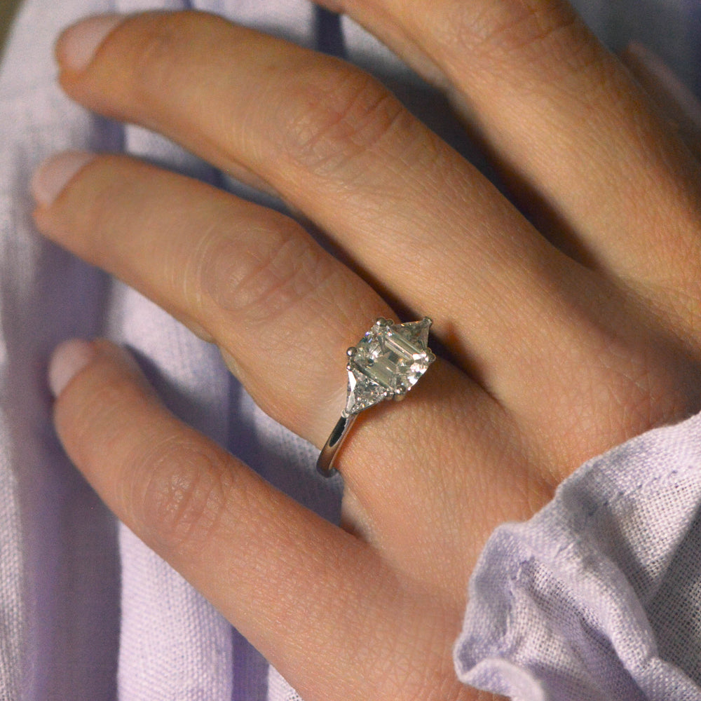 Trilogy diamond engagement ring worn on a hand with lilac linen in the background