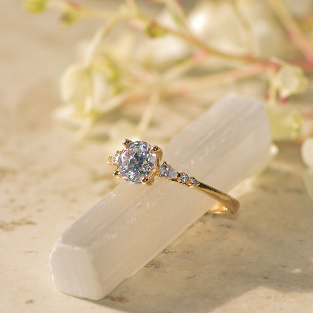 Gold diamond engagement ring with a diamond on a white stone with blurred natural background