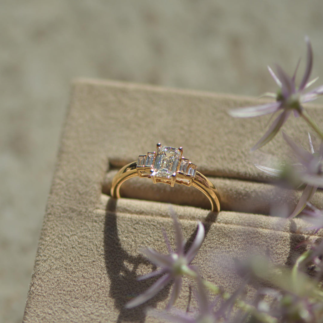 Close up of a gold engagement ring set with an emerald cut lab grown diamond inspired by vintage Art Deco rings. 
