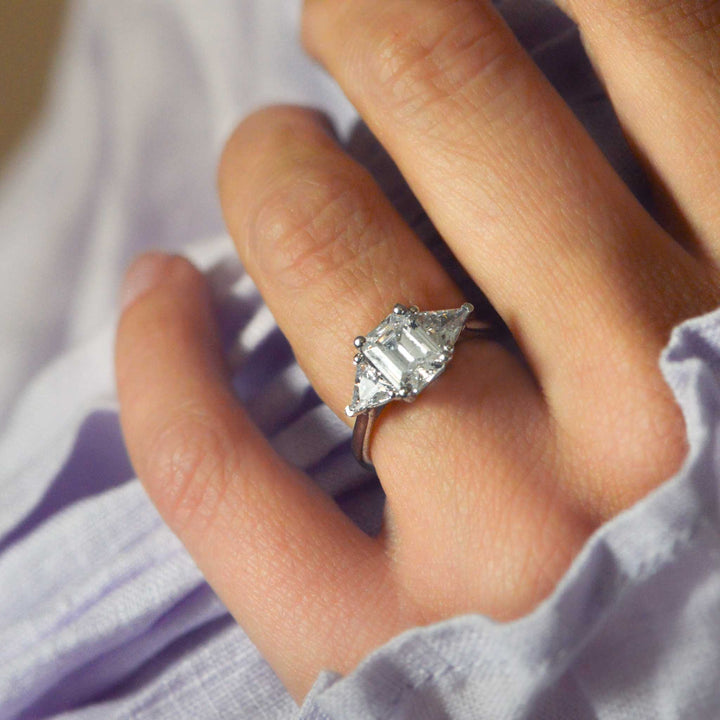 Close-up of a hand wearing an Art Deco diamond ring with a light purple fabric background