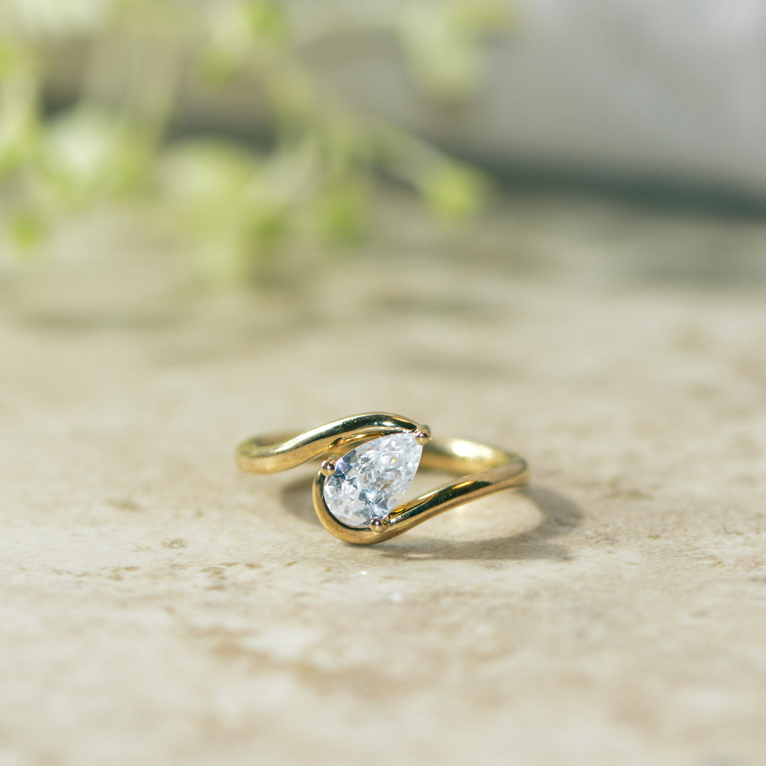 Gold solitaire ring with a pear cut diamond on a beige surface