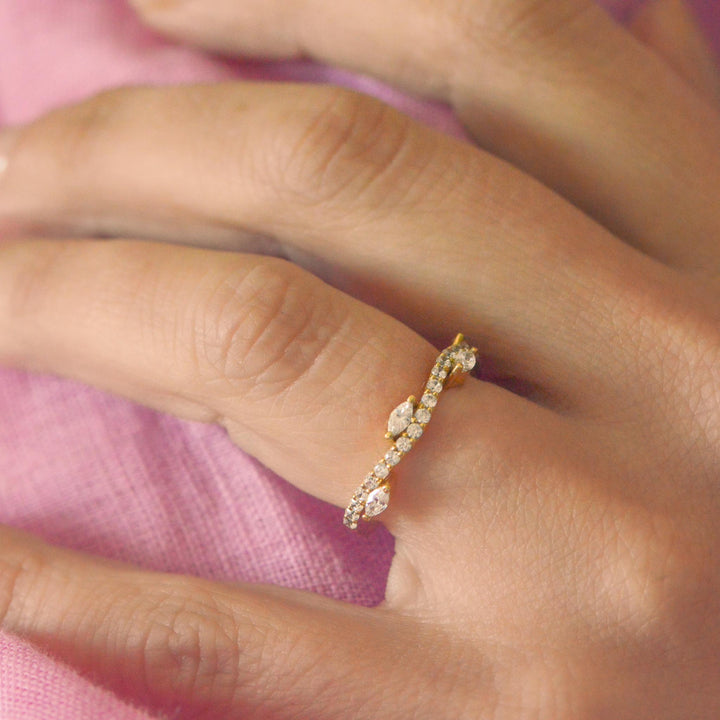 Gold ring with small diamonds on a person's finger against a pink fabric background