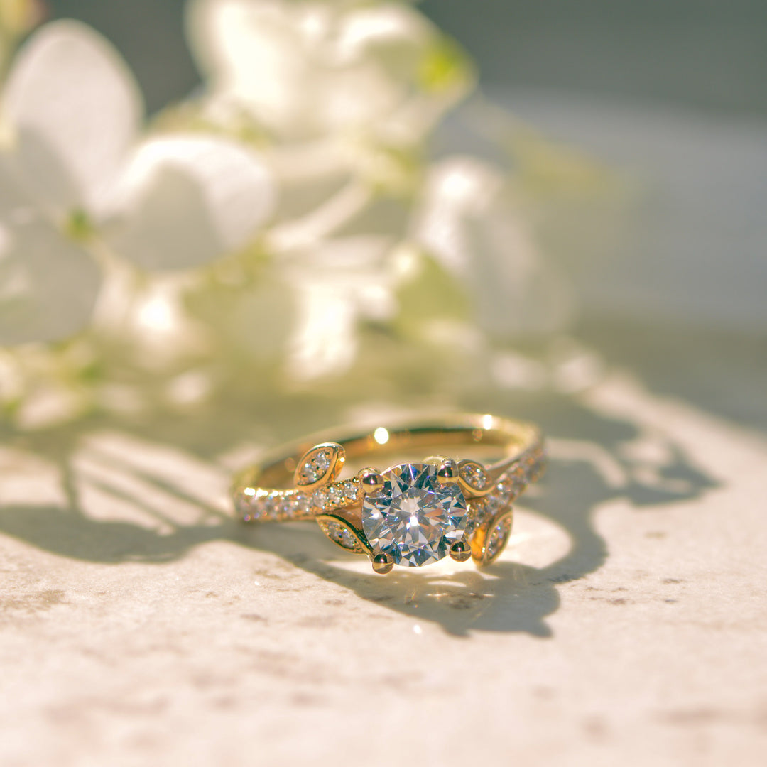 Gold nature inspired ring with a diamond on a marble surface with white flowers in the background