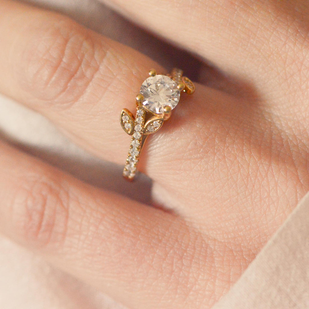 Nature inspired gold engagement ring with a round brilliant cut diamond on a finger
