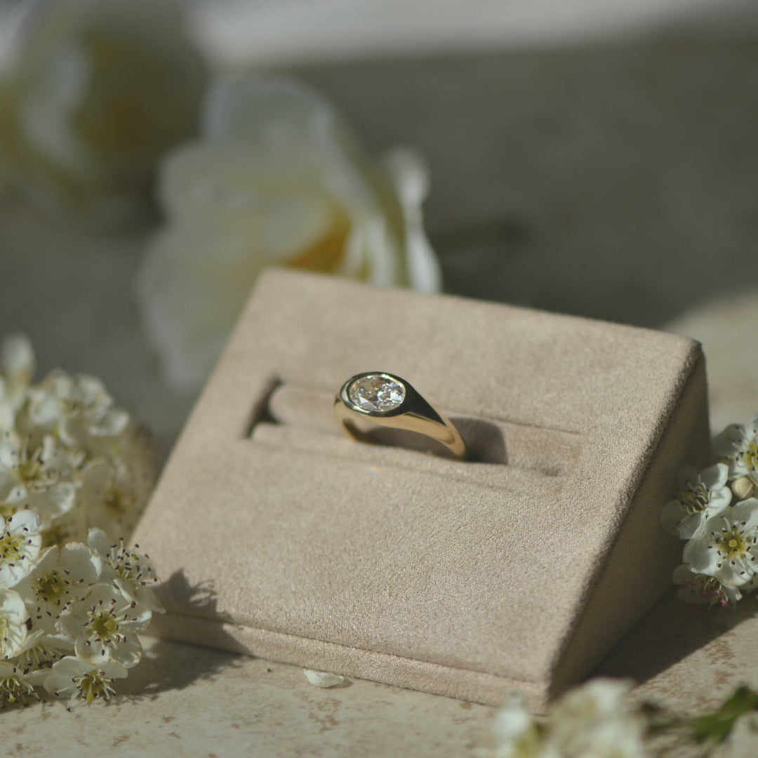 Bespoke oval cut diamond signet ring in a neutral display with flowers