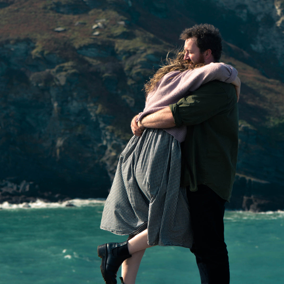 Two people embracing on a cliff overlooking the ocean