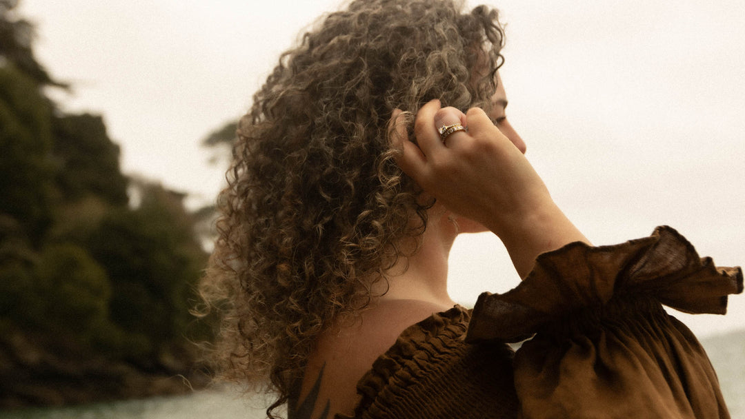 Person with curly hair wearing a lab diamond engagement ring in gold, on the beach