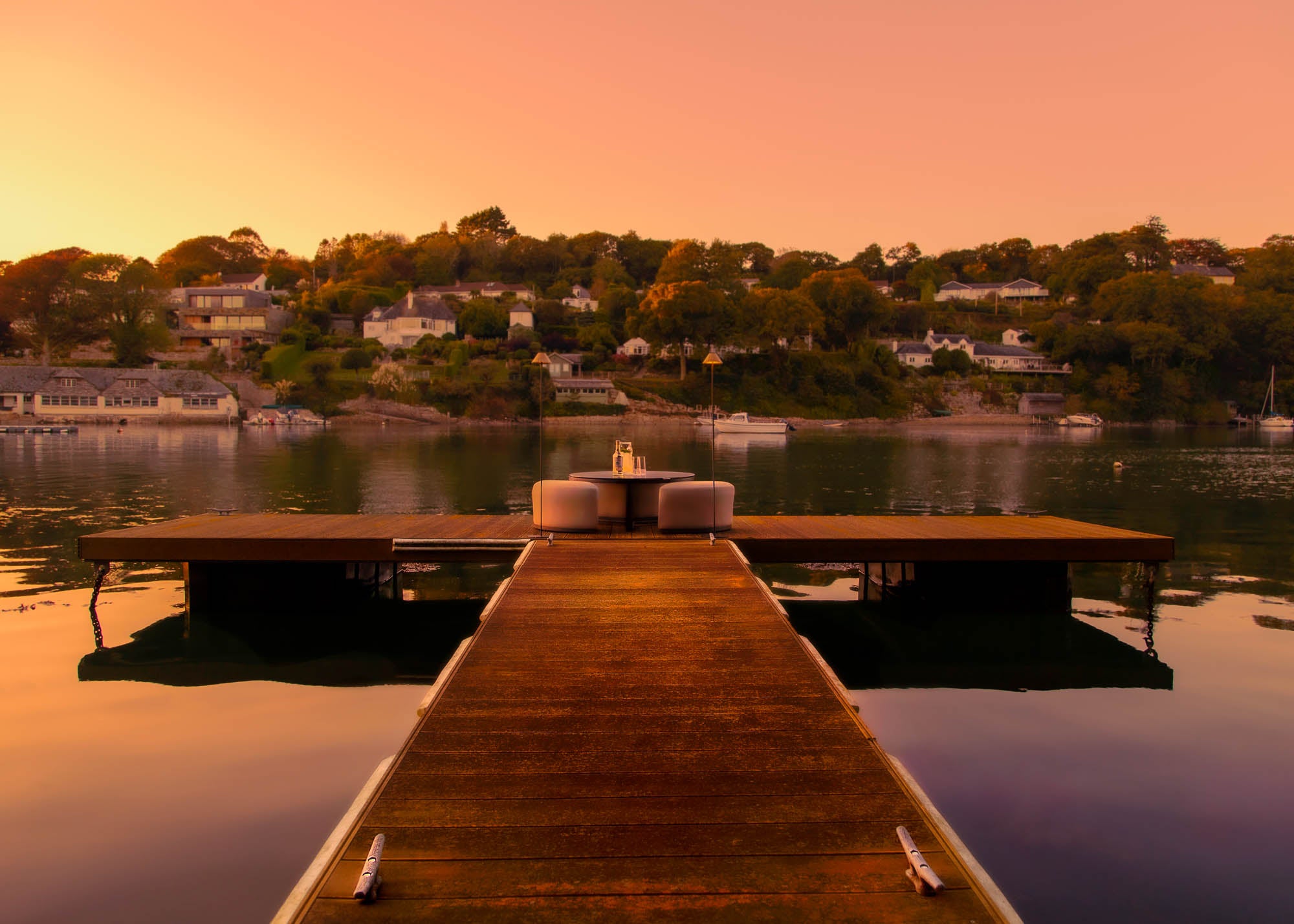 Wooden dock extending into a Cornish estuary with a sunset over.