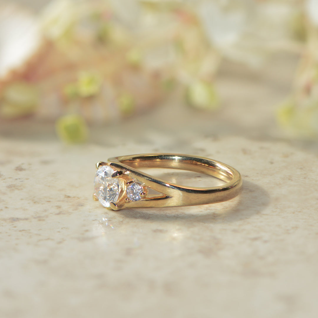 Gold engagement ring set with three round diamonds on a marble surface