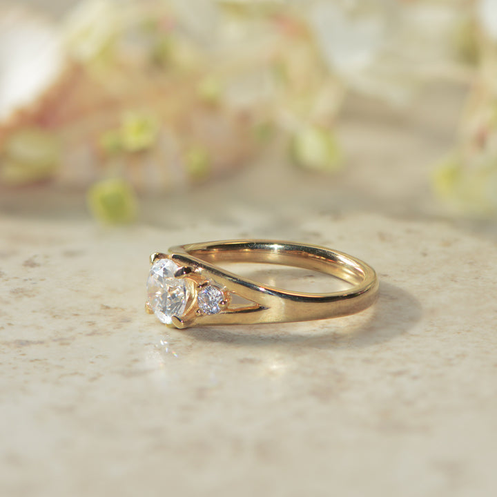 Gold engagement ring set with three round diamonds on a marble surface