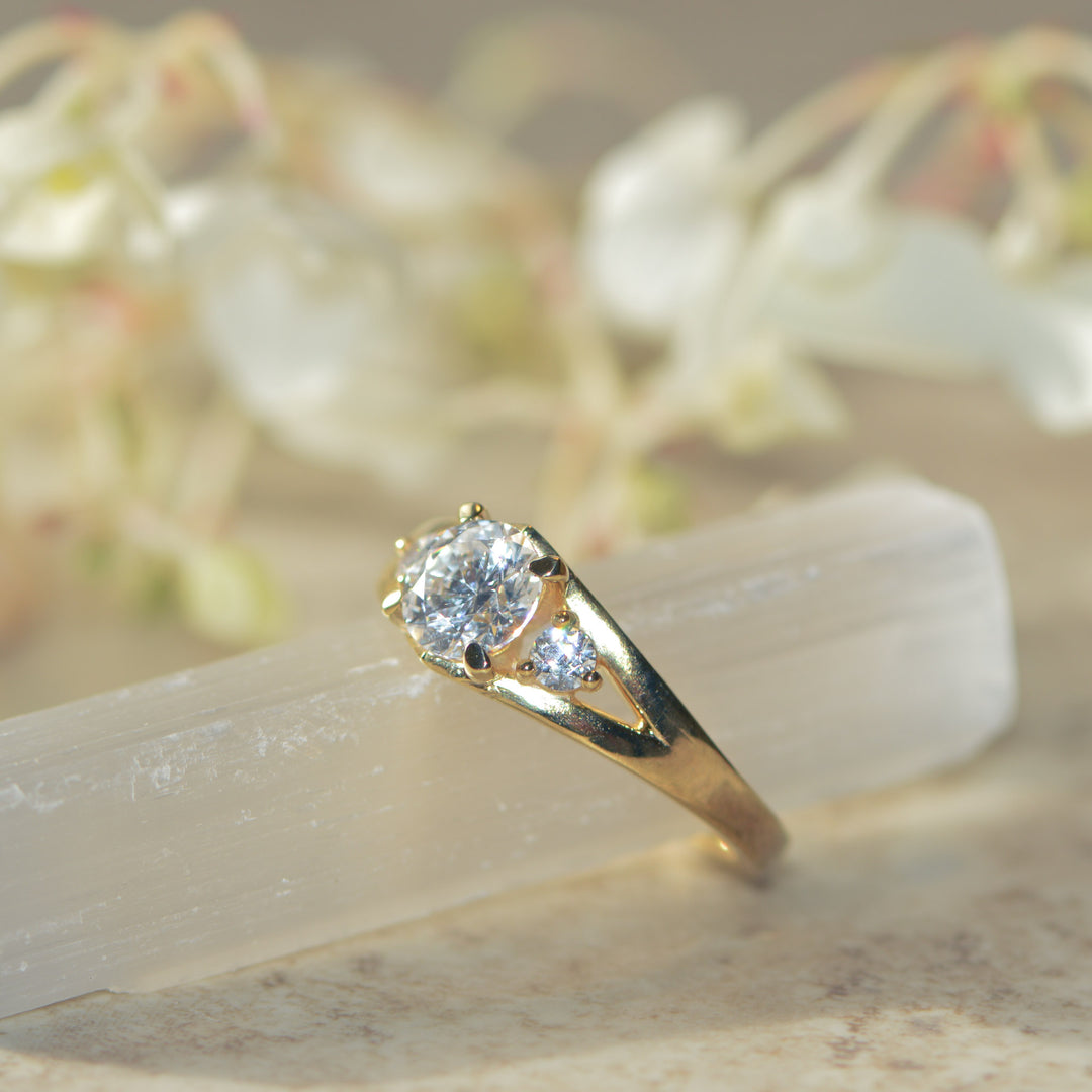 Gold & diamond trilogy ring on a white crystal with a blurred floral background