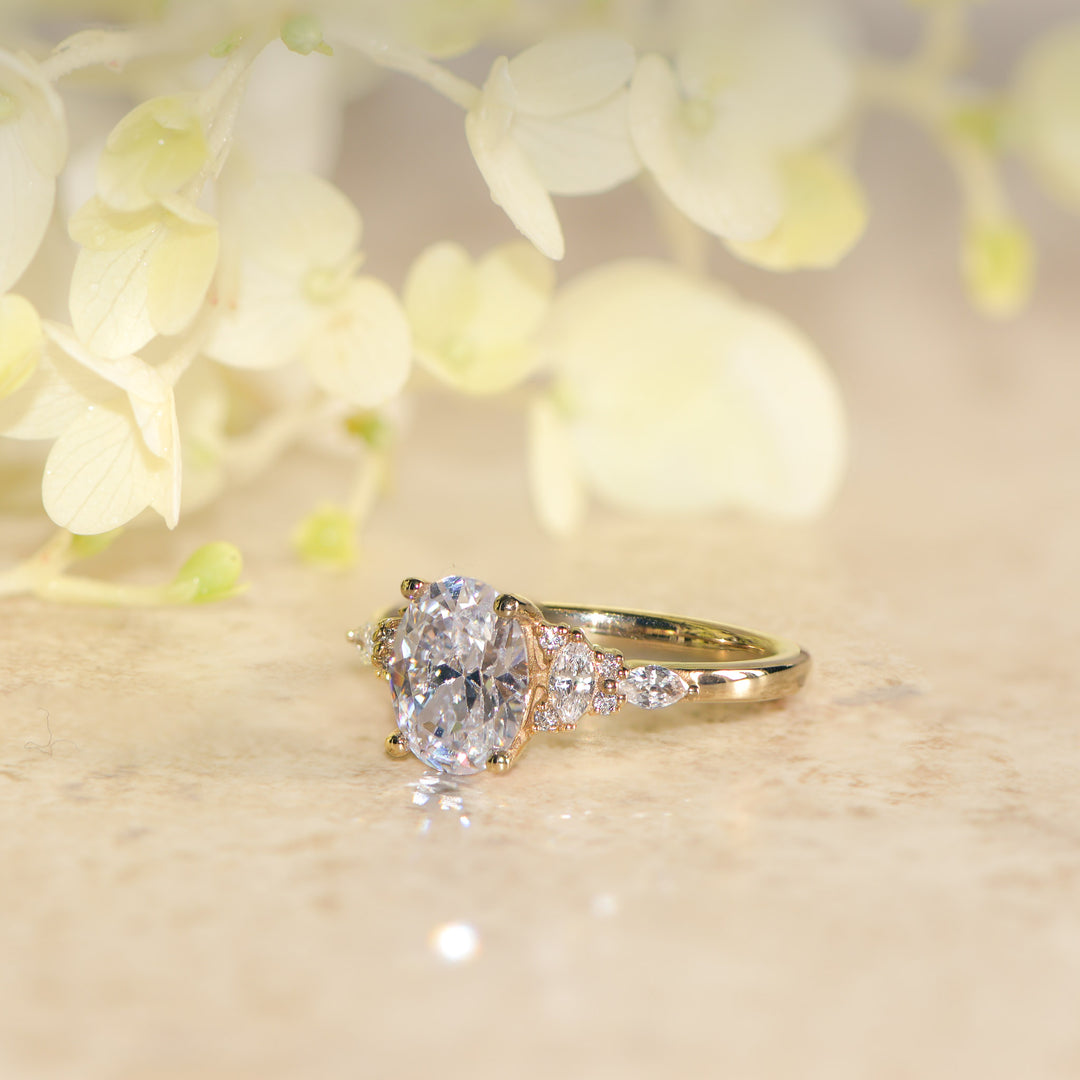 Oval cut diamond ring on a light surface with blurred flowers in the background