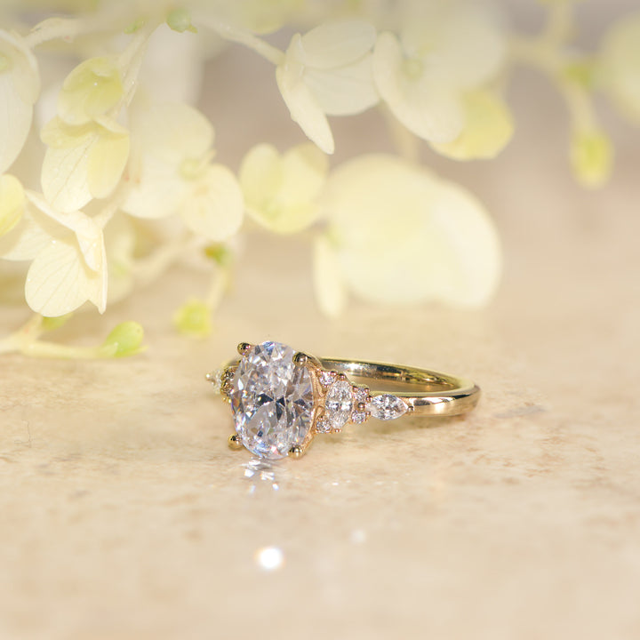 Oval cut diamond ring on a light surface with blurred flowers in the background